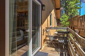 A wooden deck with a glass door leading to a room, a table with chairs, and a wooden fence. - Cozy Alpine Retreat | BBQ, Views + Fireplace (Stateline)