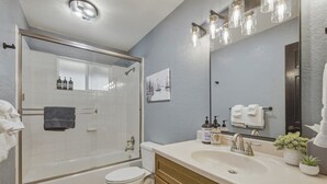 A bathroom with a glass shower enclosure, a toilet, a sink with a mirror, and toiletries. - Cozy Alpine Retreat | BBQ, Views + Fireplace (Stateline)