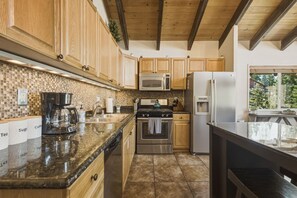 A kitchen with wooden cabinets, stainless steel appliances, a coffee maker, and a tiled backsplash. - Cozy Alpine Retreat | BBQ, Views + Fireplace (Stateline)