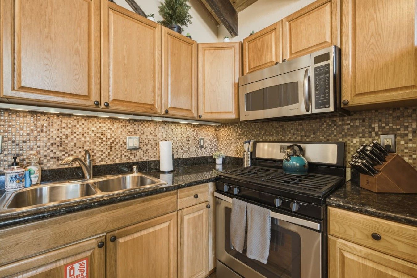 A kitchen with wooden cabinets, a stainless steel sink, a gas stove, and a microwave.