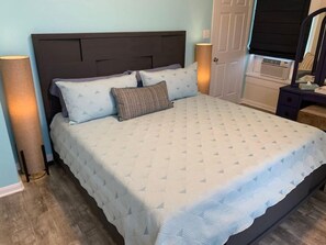 A bed with a quilted headboard, a bedside lamp, and a dresser with a mirror. - 2423 Q4 Near the Pier (Galveston)
