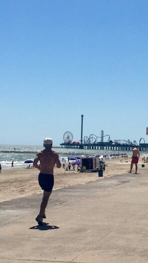 Una playa con muelle, sombrillas y gente.
