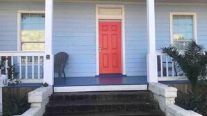 Una casa con una porta rossa, un portico e una piccola sedia.