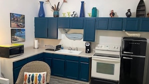 Una cucina con mobili color petrolio, un forno a microonde, una macchina per caffè, un fornello e un frigorifero.