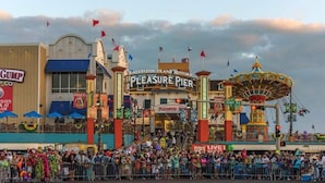 Un molo storico con una giostra, un cartello con la scritta 'Pleasure Pier' e una folla di persone.
