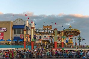 Un muelle histórico con un carrusel, un letrero que dice 'Pleasure Pier' y una multitud de gente.