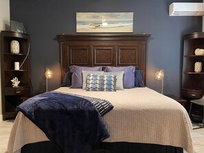 Ein Schlafzimmer mit einem großen Bett, einem Kopfteil mit aufwendigen Schnitzereien, einem Gemälde über dem Bett und zwei Nachttischlampen.