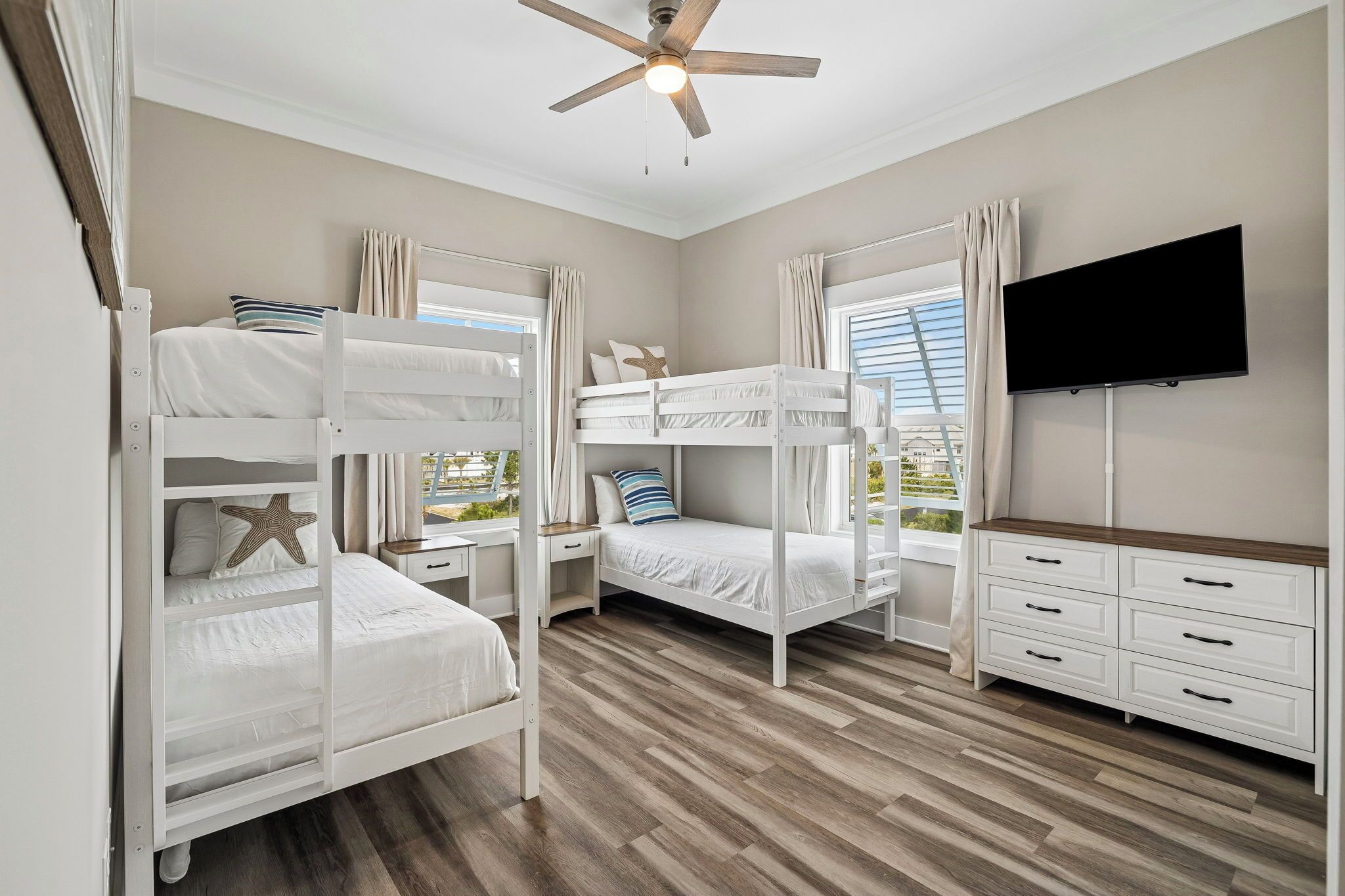 A room with bunk beds, a ceiling fan, a TV, and a view of greenery outside.