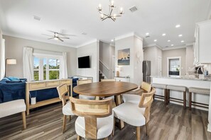 A modern kitchen with a central island, a dining area with a round table and chairs, and a living area with a sofa and a TV.