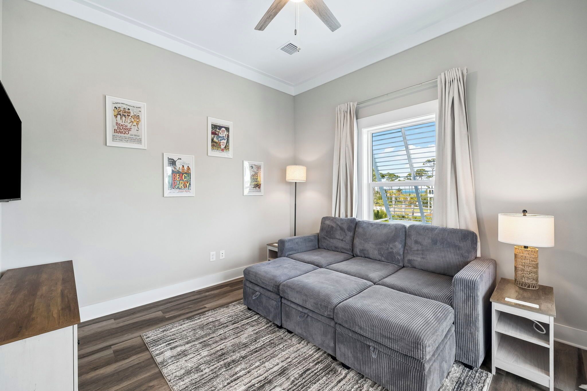 A living room with a grey sectional sofa, a floor lamp, a small side table, and a large window with curtains.