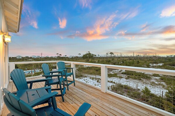 A wooden deck with chairs and a table, overlooking a natural landscape with trees and water.