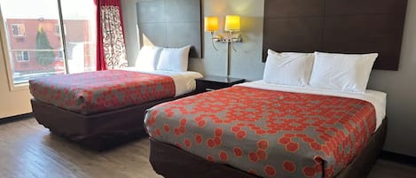 Una camera d'albergo con due letti, un'ampia finestra con tende e una lampada a muro.