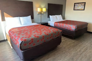 Hotellihuone, jossa on kaksi sänkyä, yöpöytä, seinään kiinnitetyt lamput ja seinällä oleva taulu.