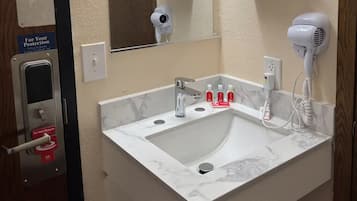 A bathroom with a white sink, a mirror, a hairdryer, and a 'Do Not Disturb' sign.