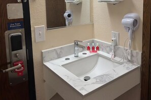 A bathroom with a white sink, a mirror, a hairdryer, and a 'Do Not Disturb' sign.