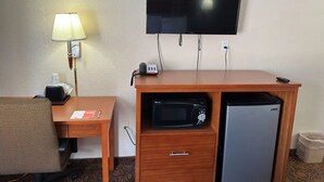 Una habitación de hotel con escritorio, lámpara, televisión, microondas y refrigerador.