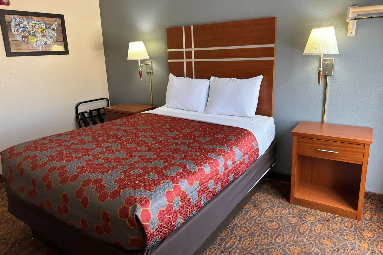 A hotel room with a bed, two bedside tables, a chair, and a wall-mounted lamp.