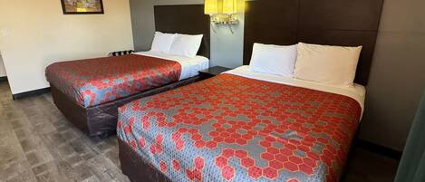 Two beds with matching red and blue patterned bedspreads, a dark headboard, a wall-mounted light fixture, and a framed picture on the wall.