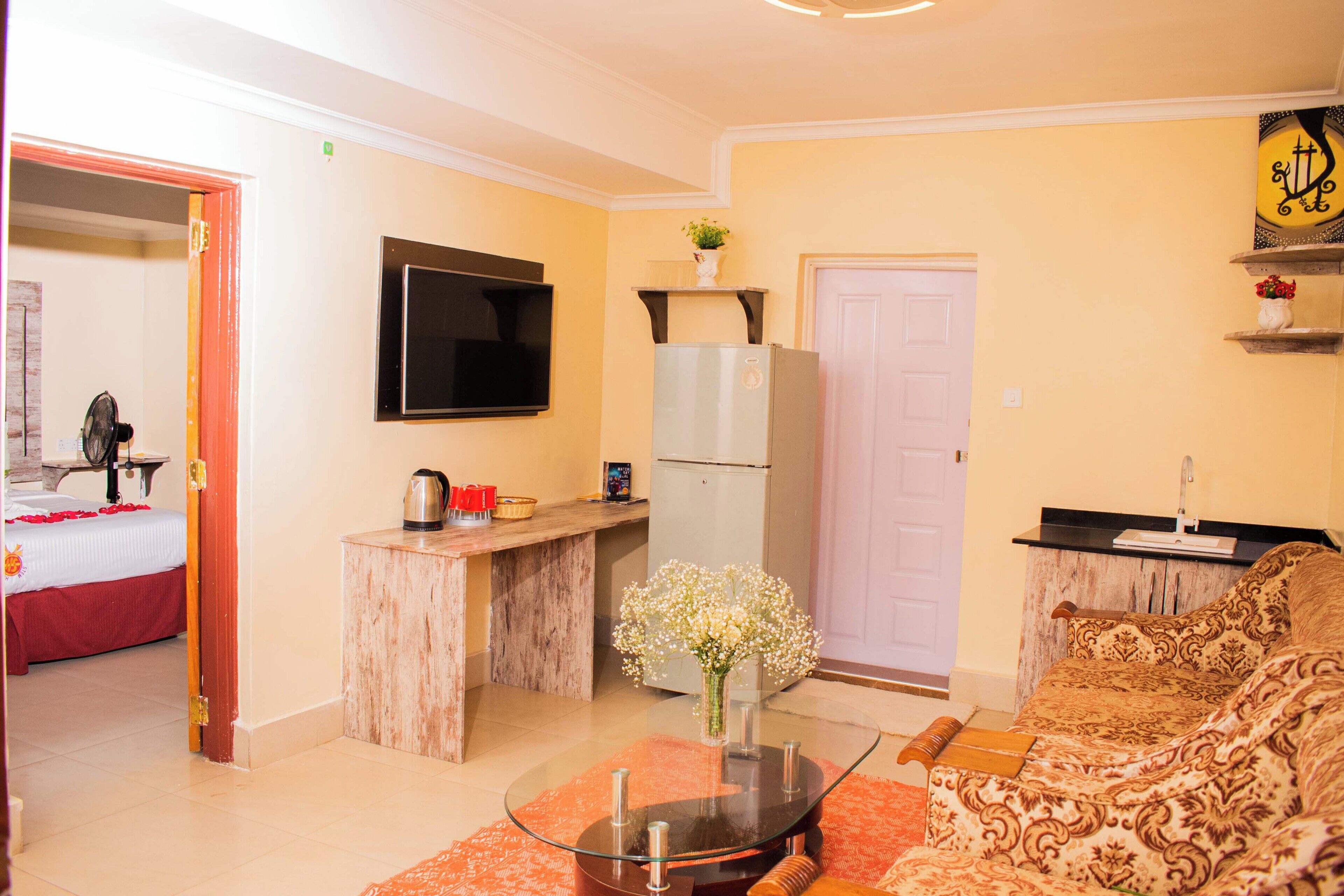Un espacio habitable compacto con kitchenette, un sofá, un televisor y una cama con colcha roja.