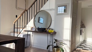 A staircase with a wooden handrail and black balusters, a round mirror on the wall, a desk with a computer and a yellow bowl, a potted plant, and a checkered floor. - Luxury Urban Retreat with Private Rooftop Views of Manhattan (Hoboken)