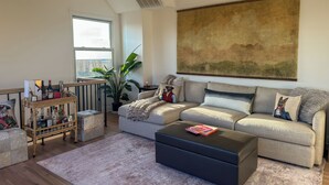 A living room with a sofa, coffee table, and a large painting on the wall. - Luxury Urban Retreat with Private Rooftop Views of Manhattan (Hoboken)