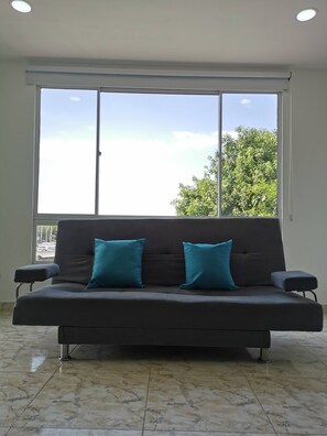 A dark-colored sofa with teal cushions in a room with a large window, marble floor, and a ceiling light. - Elegante apartamento familiar Edimar 302 (Magdalena)