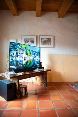 A television on a wooden stand with a tiled floor and a ceiling with exposed beams. - Art Filled Adobe Casita, where the mountains and the desert meet. (Taos)