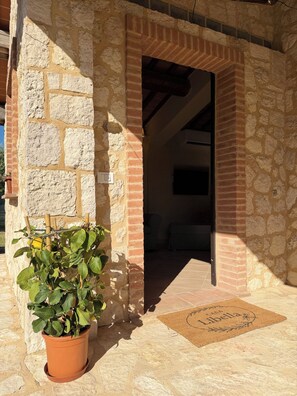 A stone and brick building entrance with a potted plant, a doormat, and a visible room with a bed. - Casa Libella - A Pool, Nature, and Tuscan Charm Near Volterra (Toscana)
