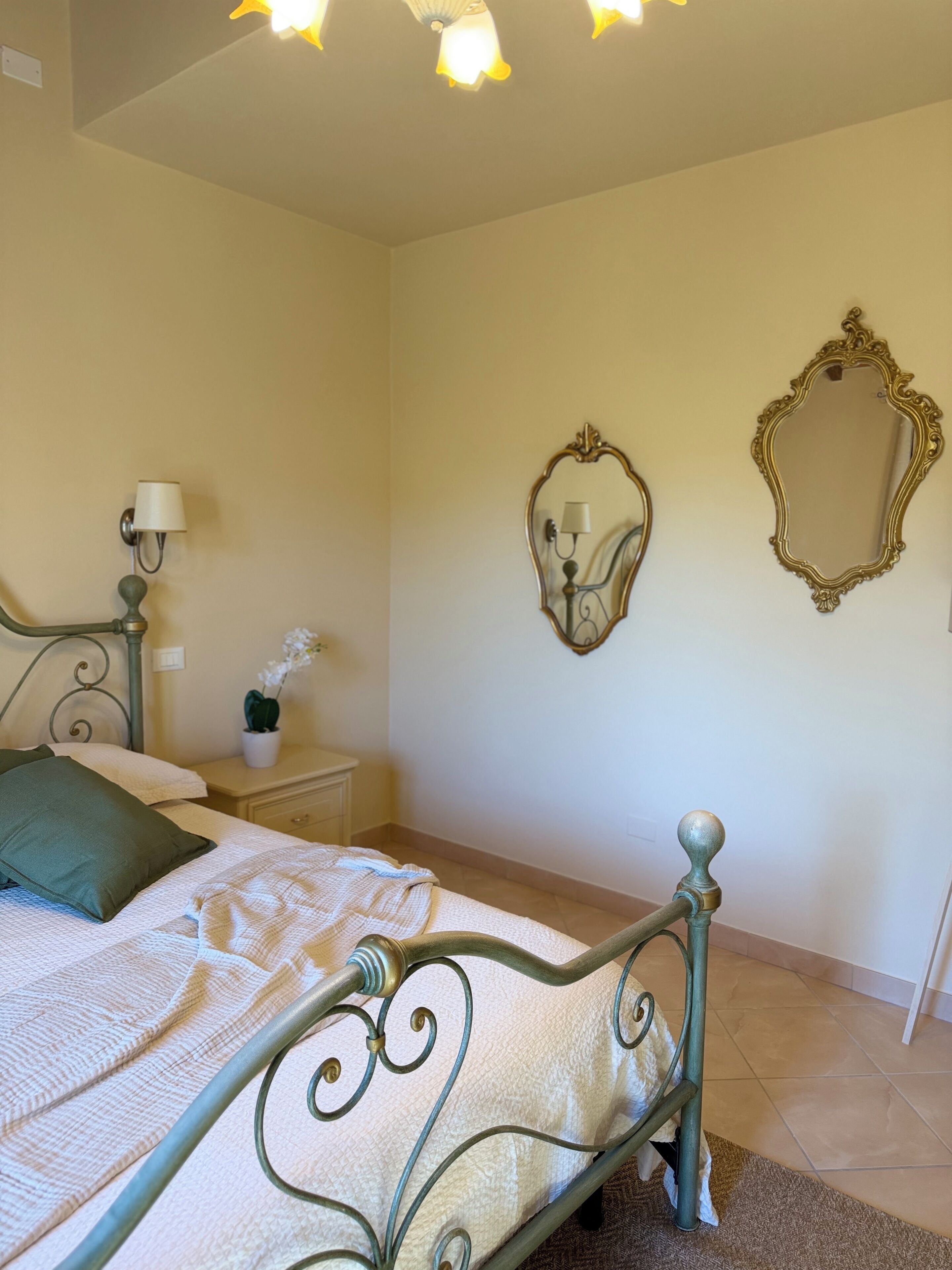 A bedroom with a bed, a nightstand, a lamp, a mirror, and a ceiling light fixture.