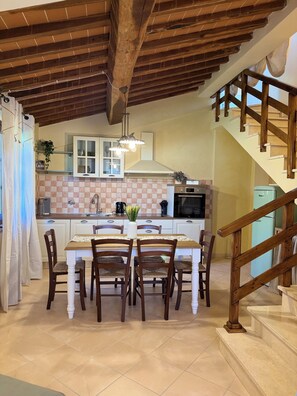 A kitchen with a dining table, chairs, a hanging light fixture, and a staircase. - Casa Libella - A Pool, Nature, and Tuscan Charm Near Volterra (Toscana)