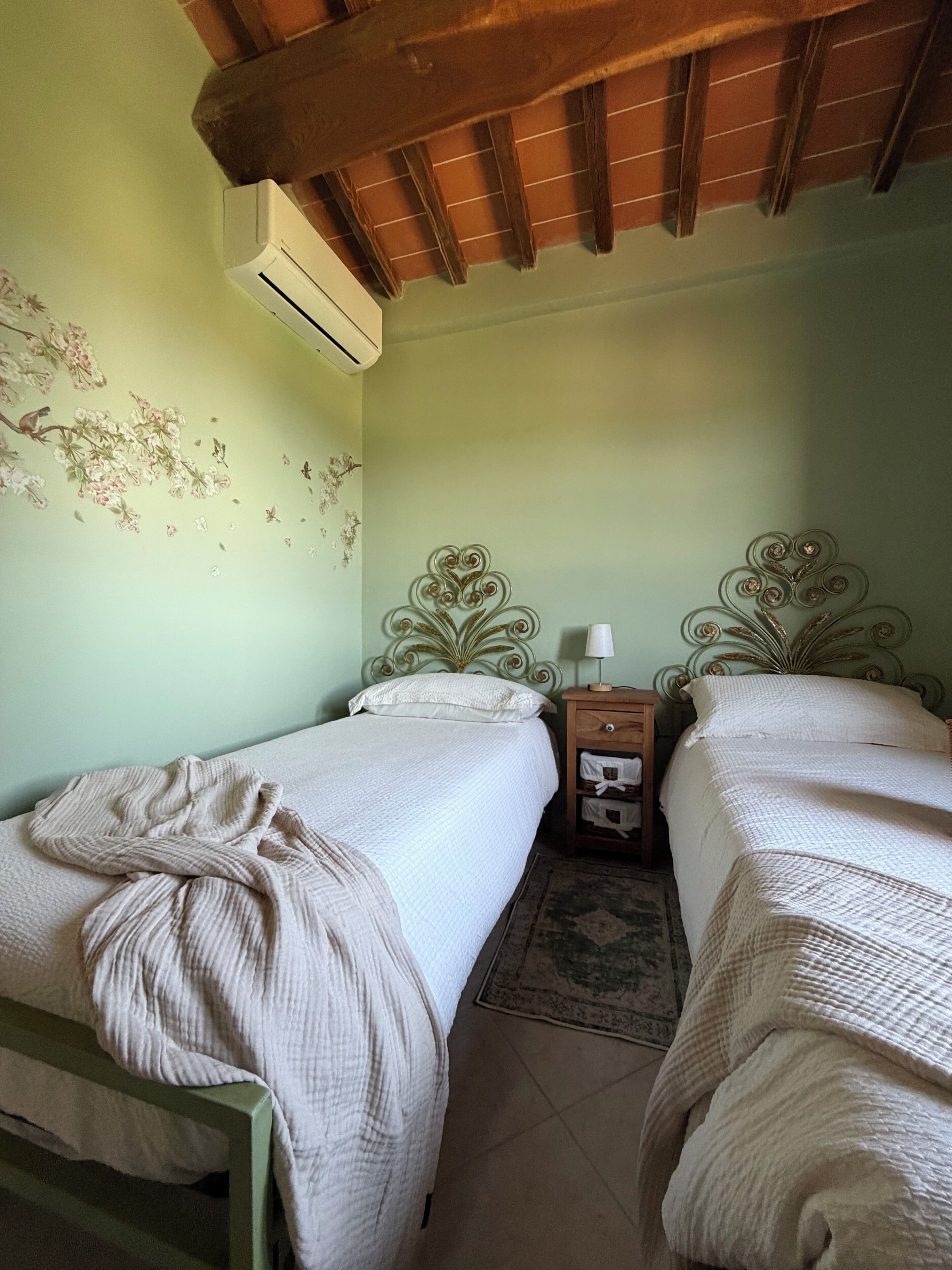 Een kamer met twee bedden, een nachtkastje, een ingebouwde airconditioning en een decoratief wandobject.