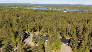Une vue aérienne d’une zone boisée comprenant plusieurs bâtiments, notamment des cabanes et une maison, le tout entouré d’arbres denses et de lacs.