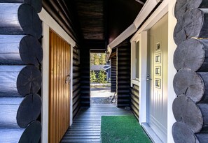 A log cabin with a wooden exterior, a green mat at the entrance, and a door with a window.