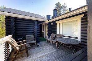 Een vakantiehuisje van hout met een houten terras, twee stoelen en een tafel.