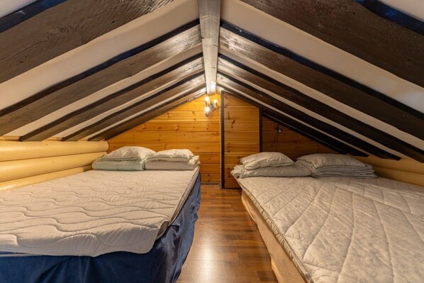 A cozy attic bedroom with two beds, wooden walls, and a sloped ceiling.