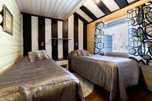 Een kamer met twee bedden, een klein tafeltje, een raam met decoratieve gordijnen, en een muur met een zwart-wit streepdessin.