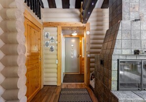 A log cabin interior with a wooden door, a fireplace, and a hallway leading to a door.