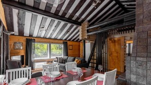 A dining area with a wooden table set for four, white chairs, and a view of the outdoors through large windows.