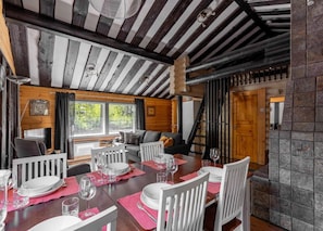 Een eetgedeelte met een houten tafel voor vier personen, witte stoelen en uitzicht op de omgeving door grote ramen.