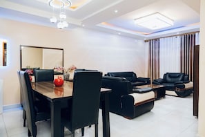 Una sala de estar moderna con comedor, sofás de cuero negro, una mesa de comedor de madera y un espejo grande.