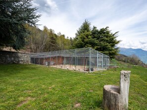 A glass-enclosed building with a stone wall, a wooden bench, and a tree stump in a grassy field. - Chalet Remondet by Interhome (Sarre)