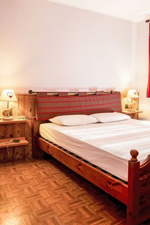 A wooden bed with a headboard, two bedside lamps, and a wooden nightstand with a lamp. - Chalet Remondet by Interhome (Sarre)