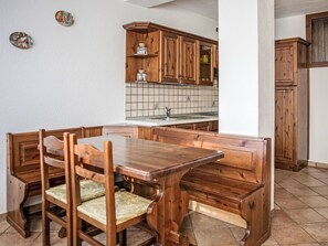 A wooden dining table with benches, a kitchen area with wooden cabinets, and a tiled backsplash. - Chalet Remondet by Interhome (Sarre)