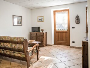 A living room with a sofa, a television on a wooden cabinet, a door with a heart-patterned curtain, and a wall-mounted clock. - Chalet Remondet by Interhome (Sarre)