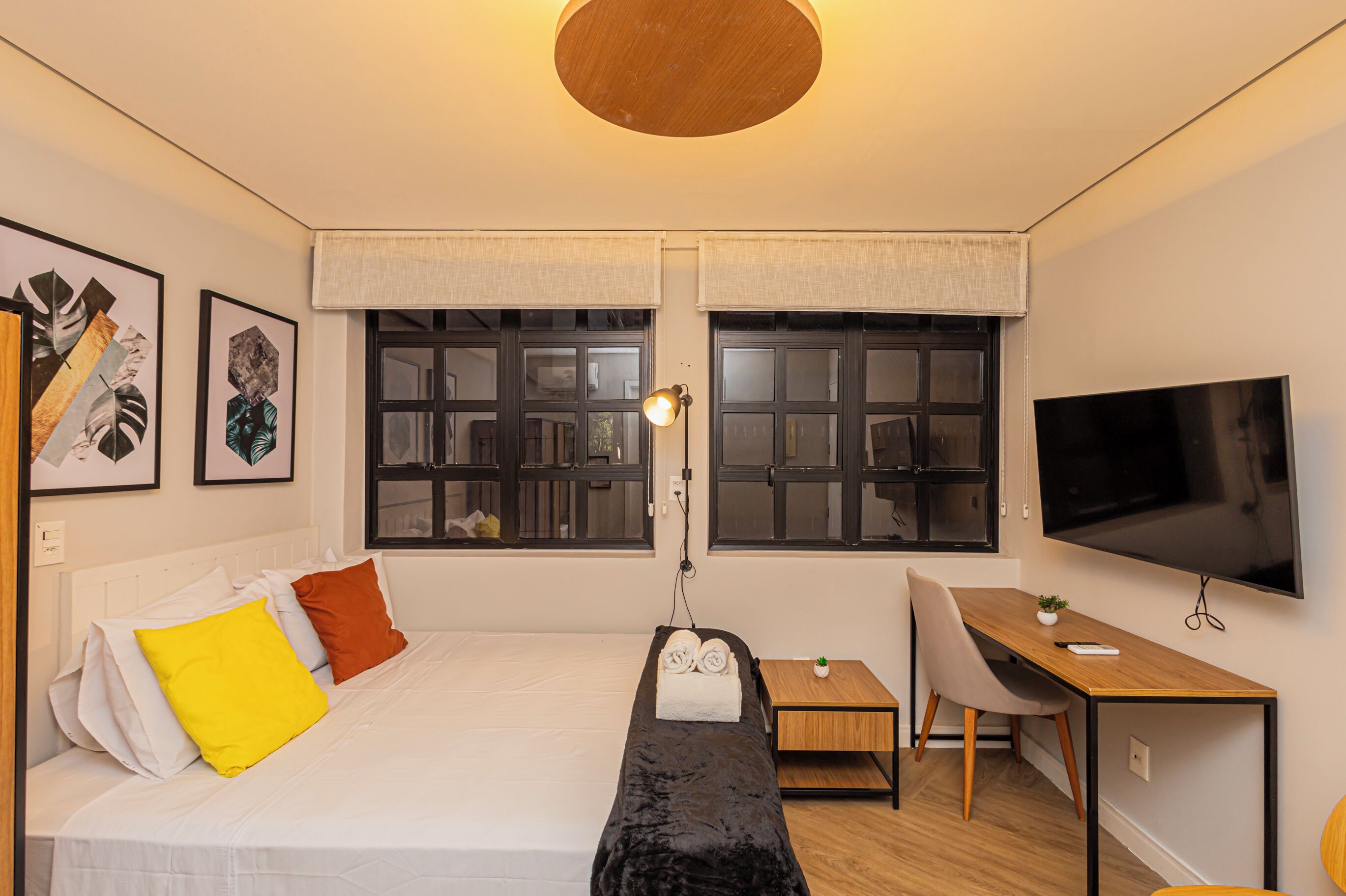 A modern bedroom with a bed, bedside table, desk, chair, and a TV.