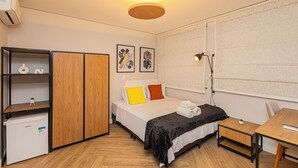 A compact hotel room with a bed, a desk, a wardrobe, and a small refrigerator. - VNM - VN Vila Olimpia by Anora Spaces (São Paulo)