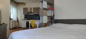 A hotel room with a bed, a desk with a chair, a kitchenette, and a wardrobe. - Piazzale Unità d'Italia 3B (Udine)