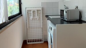 A compact kitchen with a washing machine, a microwave, and a window with a view of greenery. - Piazzale Unità d'Italia 3B (Udine)