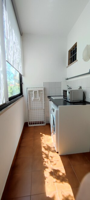 A compact kitchen with a washing machine, a microwave, and a window with a view of greenery. - Piazzale Unità d'Italia 3B (Udine)