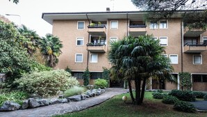 A multi-story residential building with balconies, a paved courtyard, and various shrubs and trees. - Piazzale Unità d'Italia 3B (Udine)